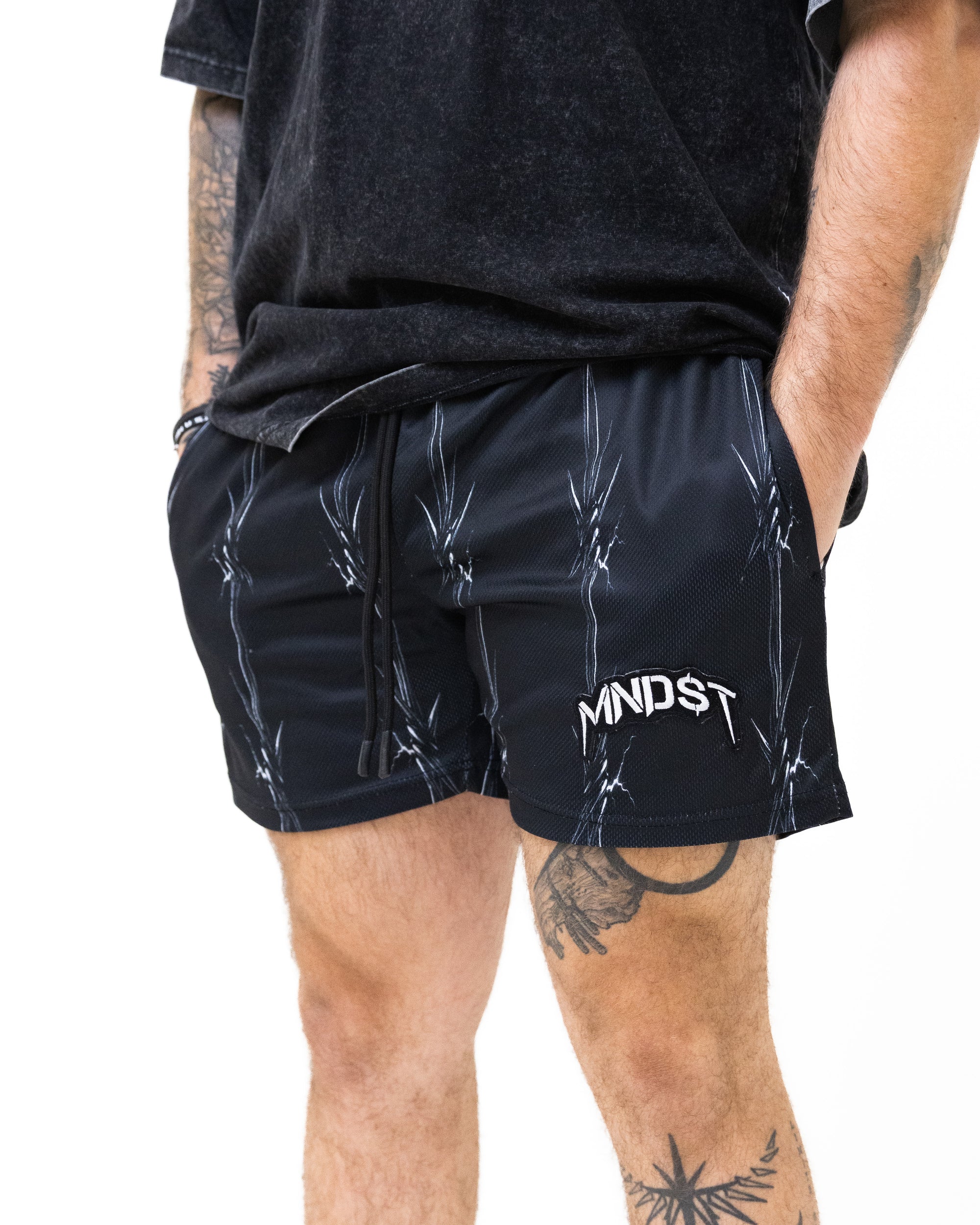 Person wearing black shorts with a visible MNDST brand logo on a white background