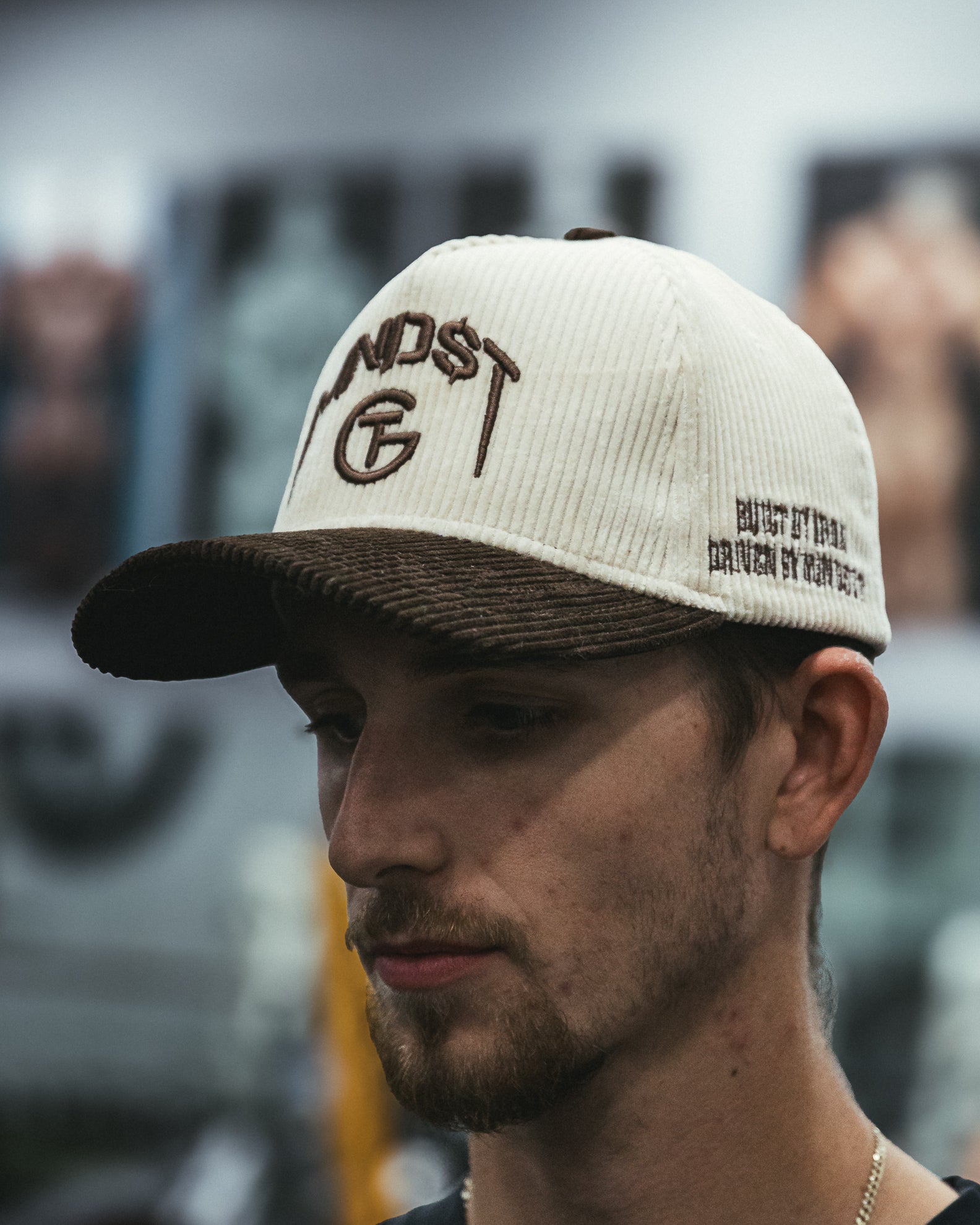 Man wearing a cream and brown corduroy MNDST TG Collab cap with text on a blurred background