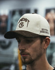Man wearing a cream and brown corduroy MNDST TG Collab cap with text on a blurred background