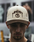 Man wearing a cream and brown corduroy MNDST TG Collab cap with text on a blurred background