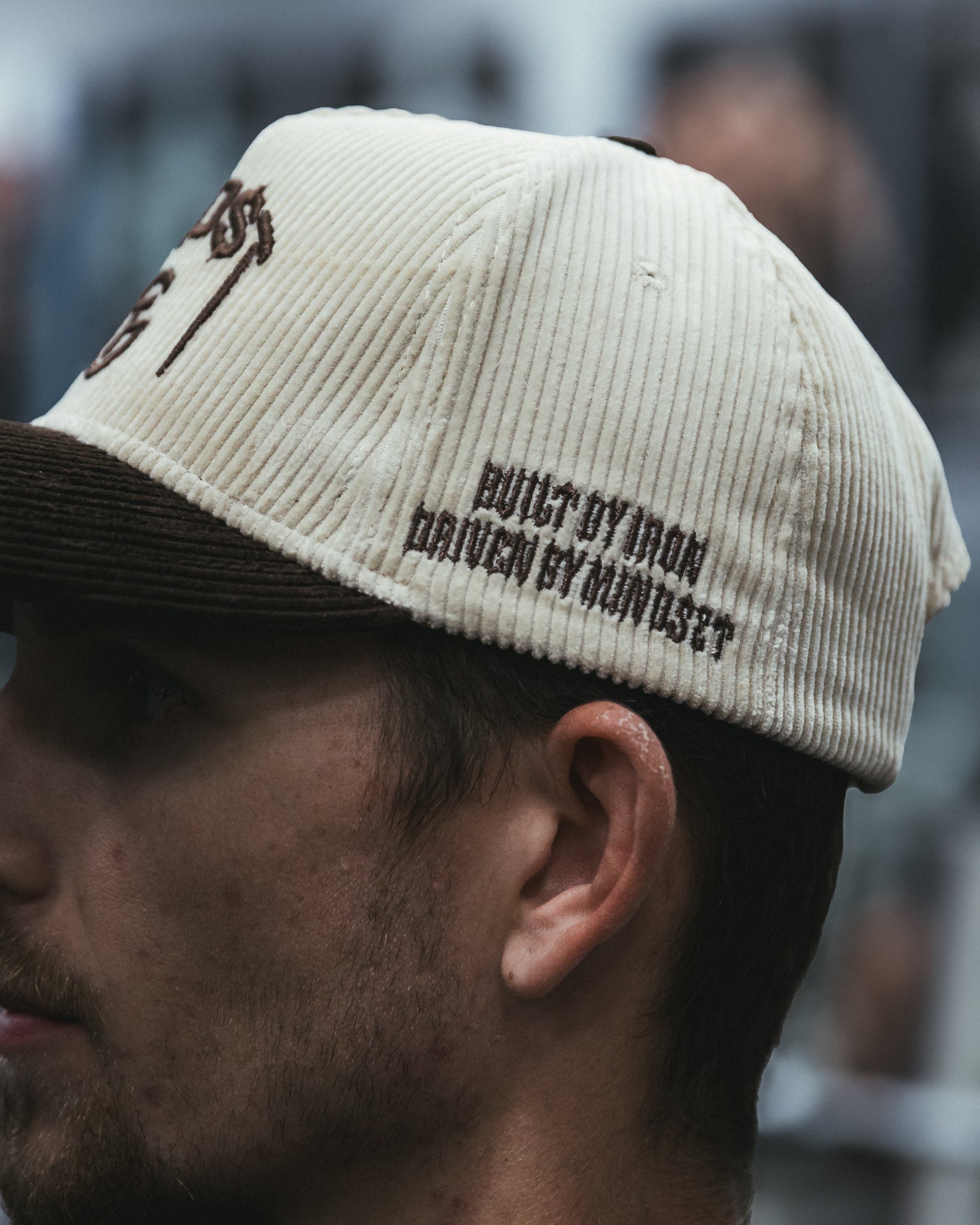 Man wearing a cream and brown corduroy MNDST TG Collab cap with text on a blurred background