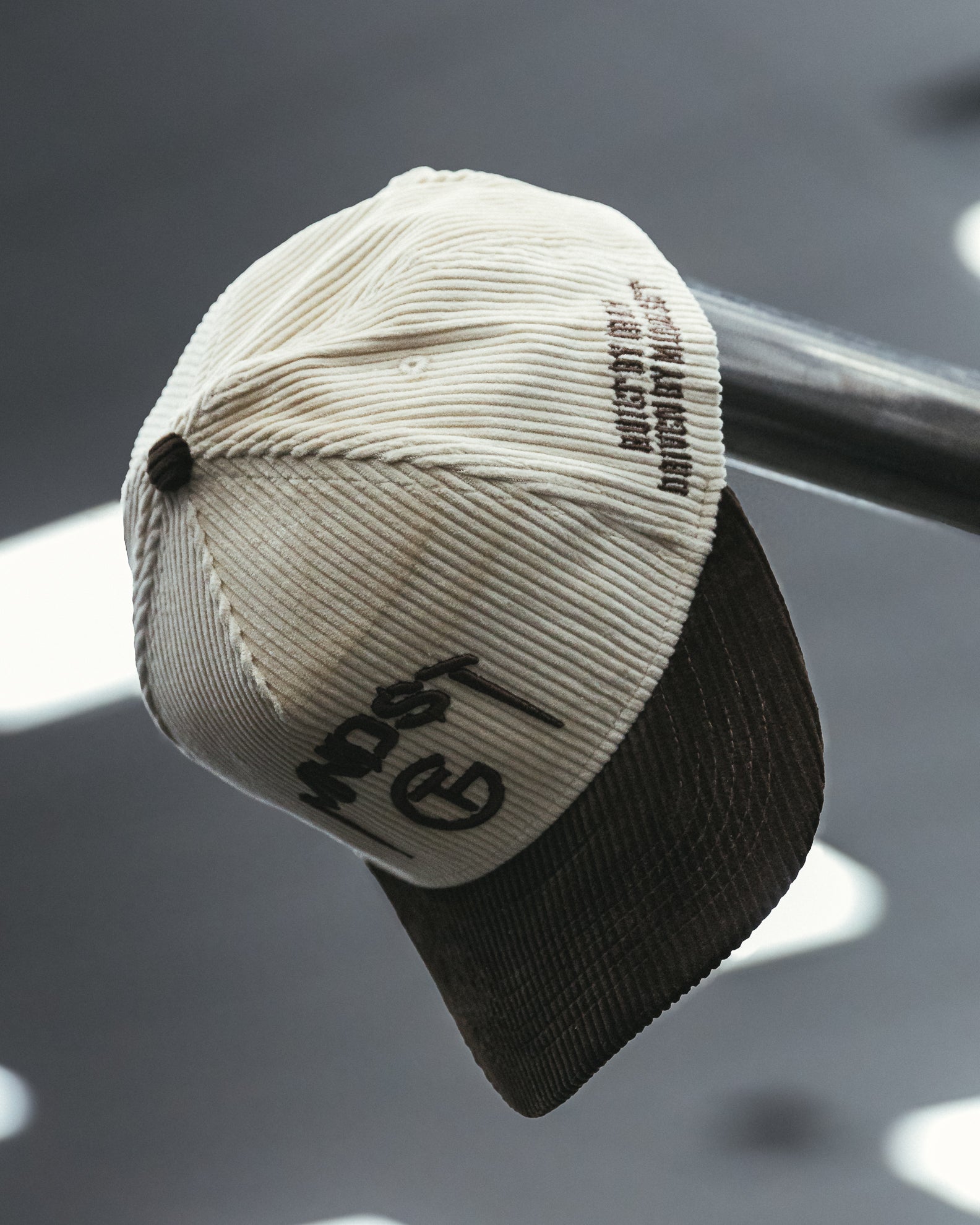 Man wearing a cream and brown corduroy MNDST TG Collab cap with text on a blurred background