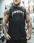 Man wearing a black sleeveless shirt or tank top with 'MNDST' logo in a gym setting
