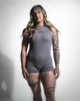 Person wearing a gray sleeveless top and shorts with visible tattoos on a white background