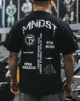 Person wearing a black t-shirt with white text and graphics, standing in front of gym equipment.
